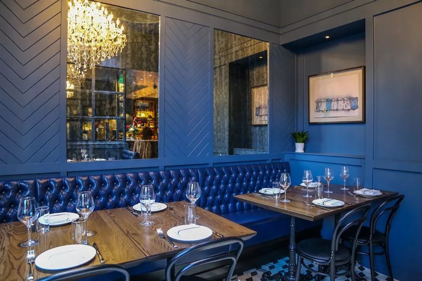 interior of a restaurant with a chandelier and blue banquette