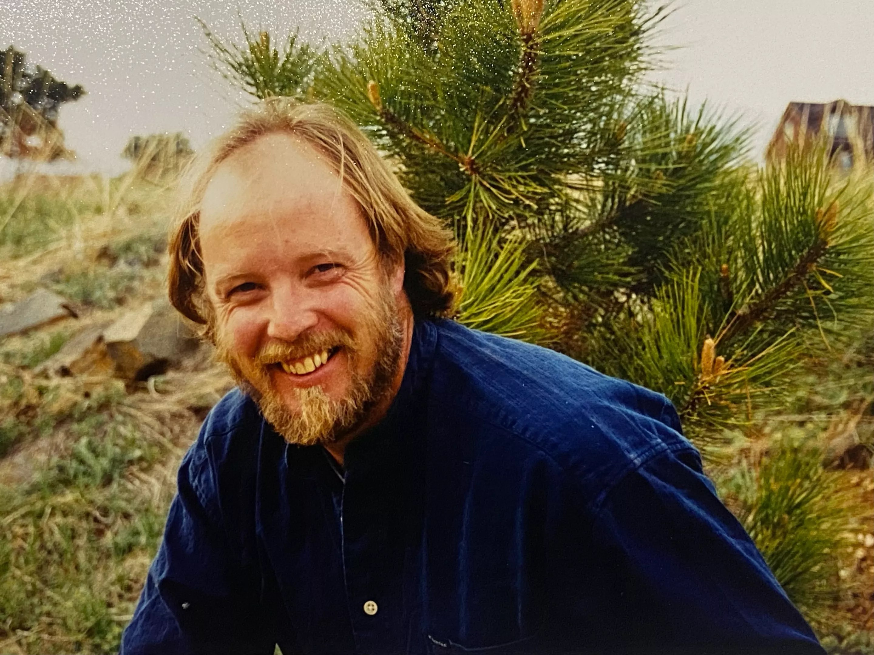 A man in a blue button up smiles at the camera.