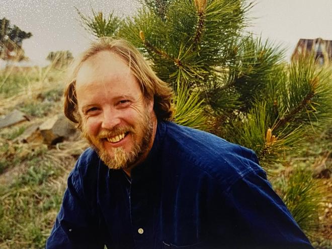 A man in a blue button up smiles at the camera.