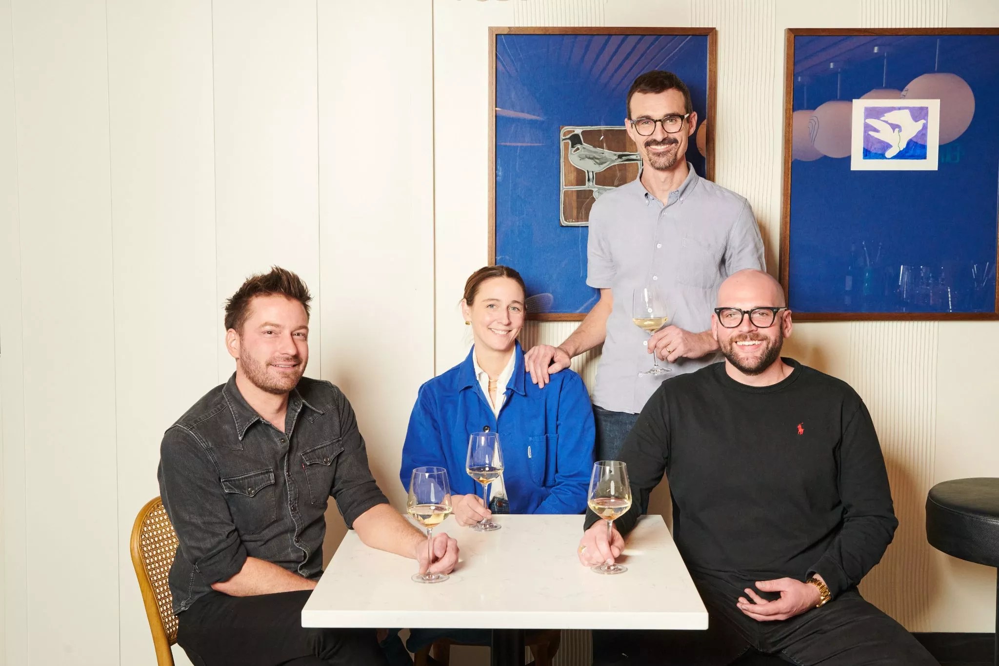 three people sitting at a white table and one standing