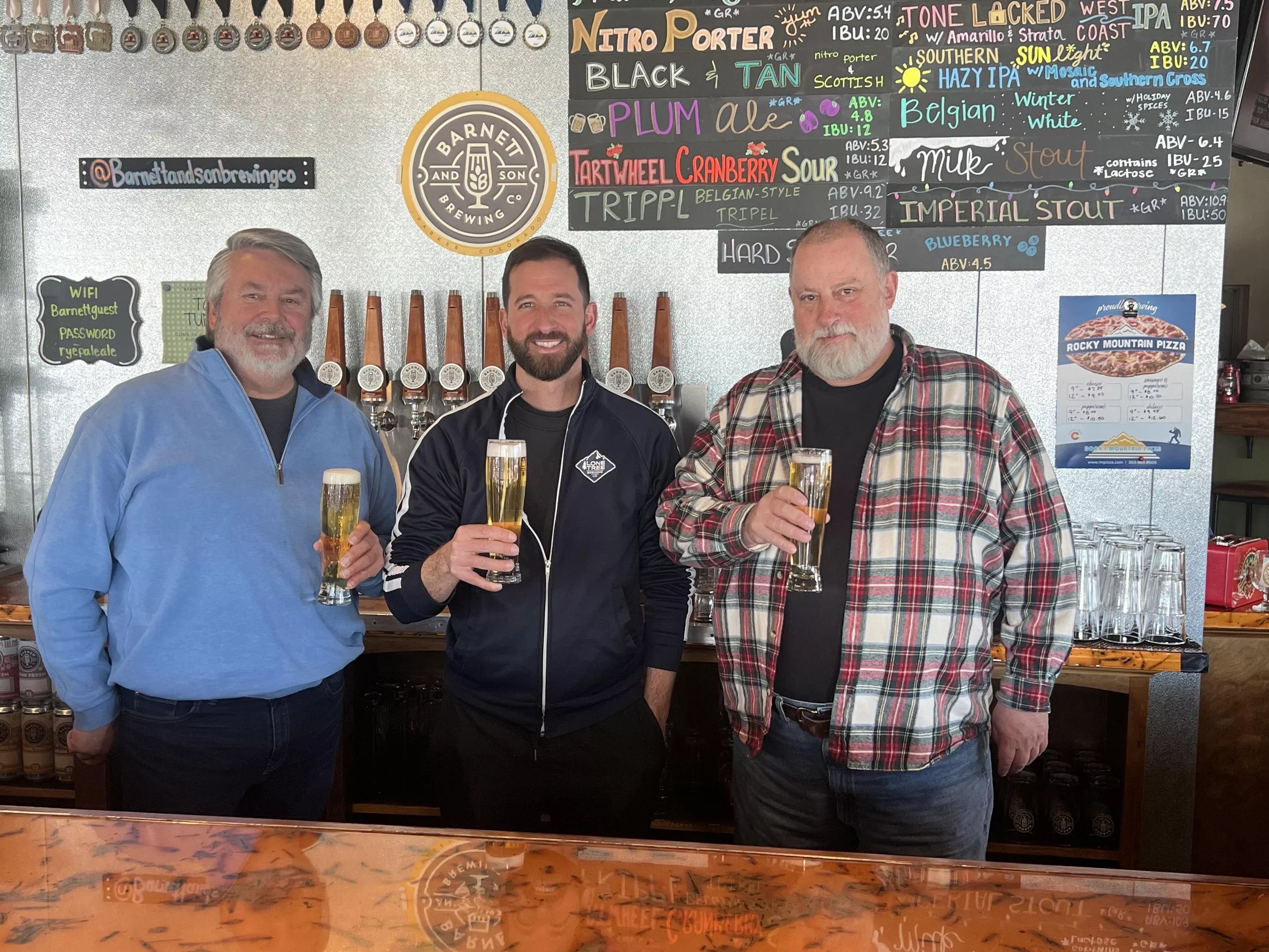 Three men standing behind a bar.