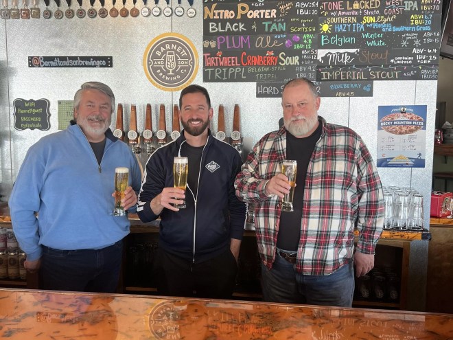 Three men standing behind a bar.