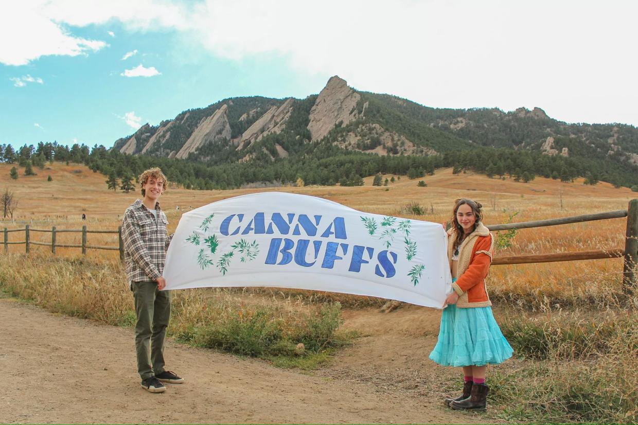College students hold a CannaBuffs banner in front of Colorado mountains