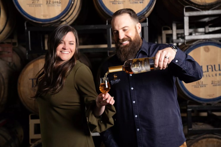 a woman holding a glass and a man pouring whiskey into it