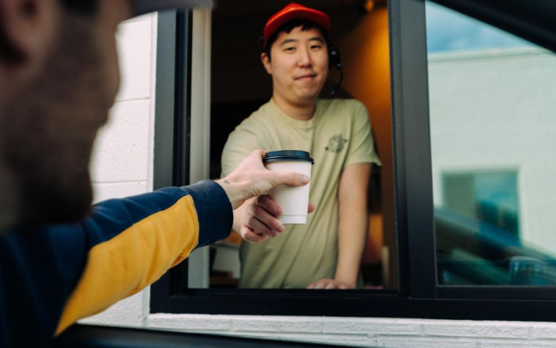 hand reaching for a cup of coffee from a drive thru