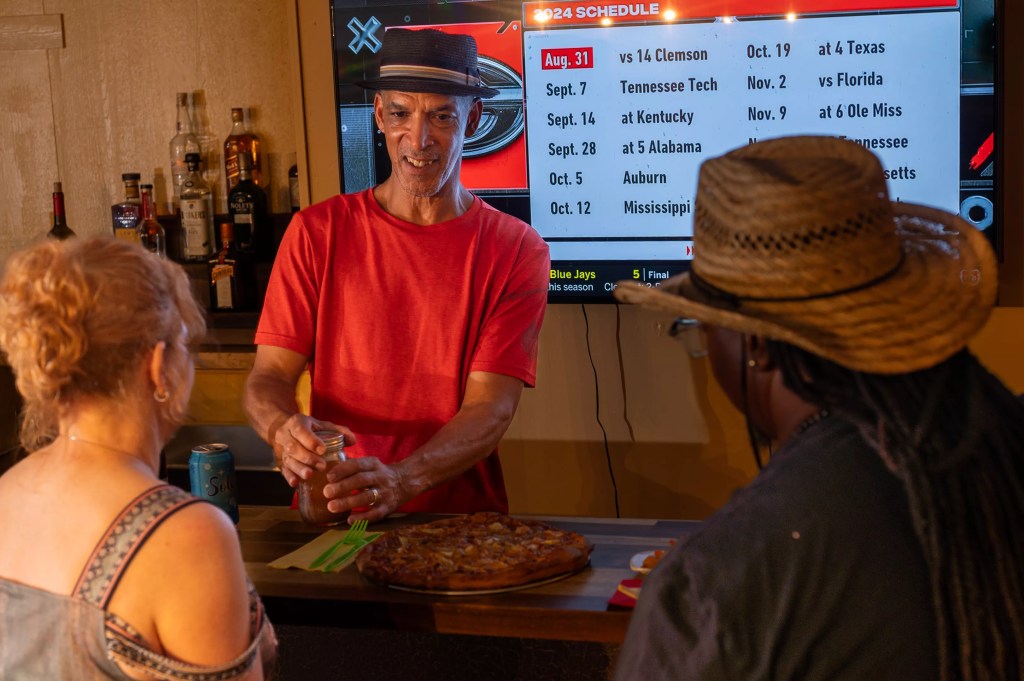 man in red shirt, black hat, in front of menu.