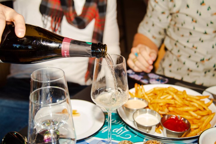champagne pouring into a glass in front of a plate of french fries.
