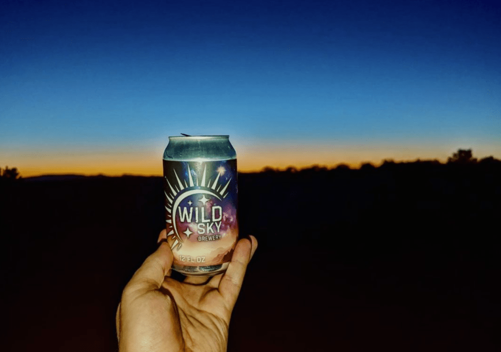 Beer can in a hand with a sunset in the background.