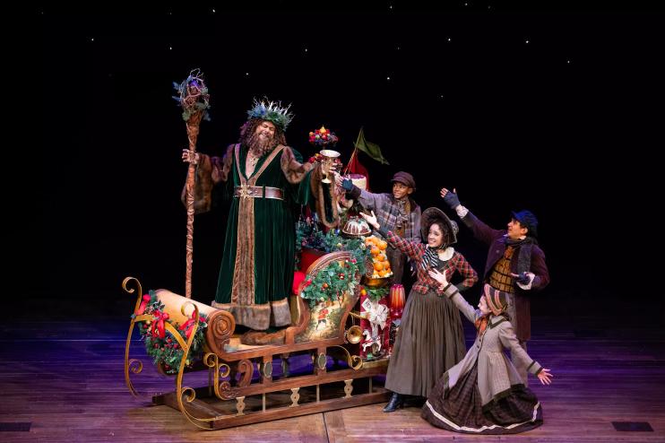A man in green rides a sleigh with people behind him.