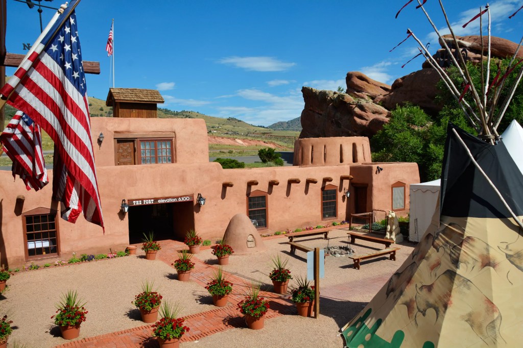 The adobe exterior of The Fort featuring a tepee and American flags