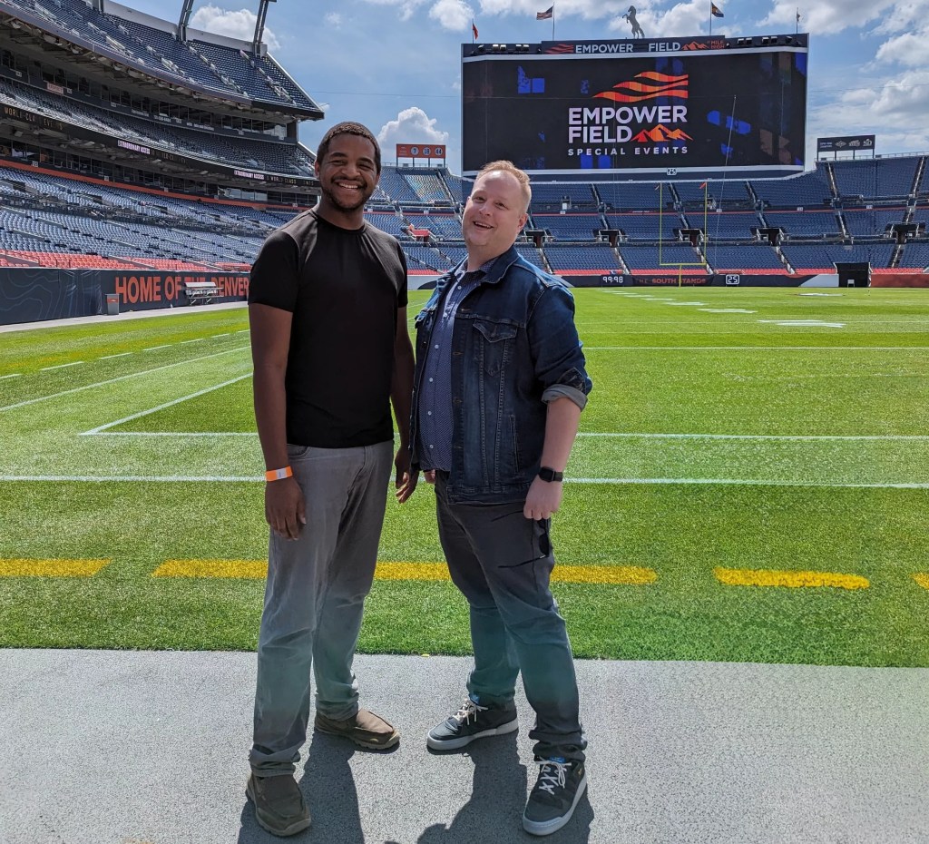 Two men stand together at Empower Field