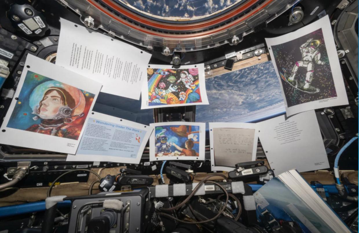 Printed out art hangs by a window looking out into the Earth's atmosphere