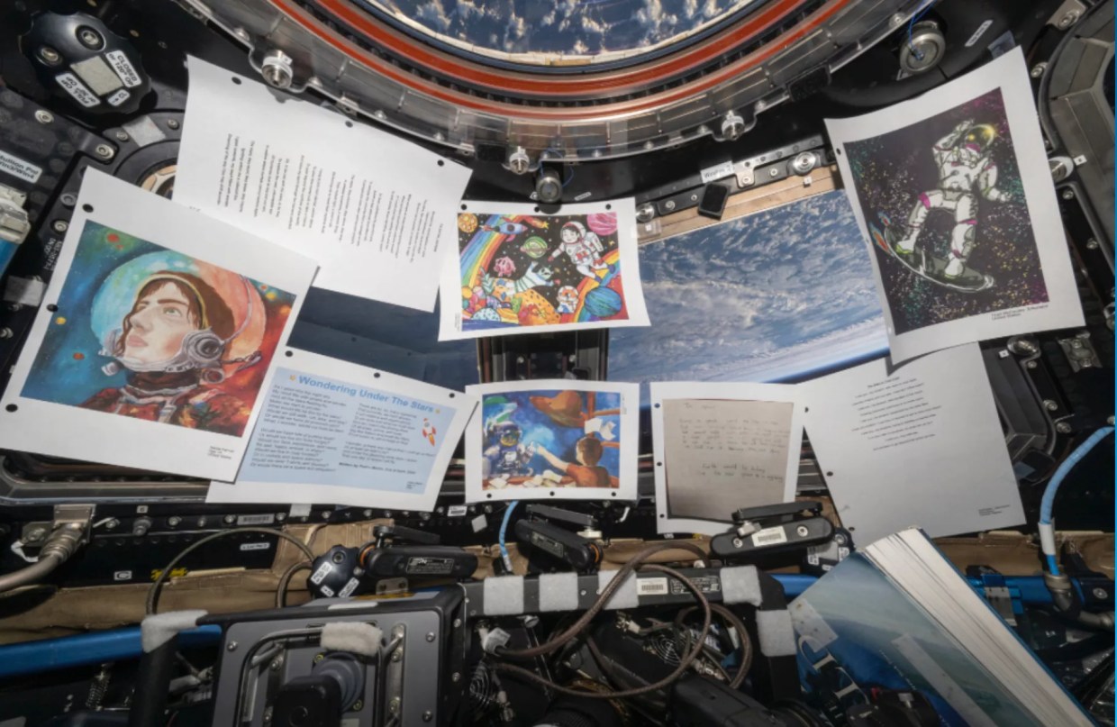 Printed out art hangs by a window looking out into the Earth's atmosphere