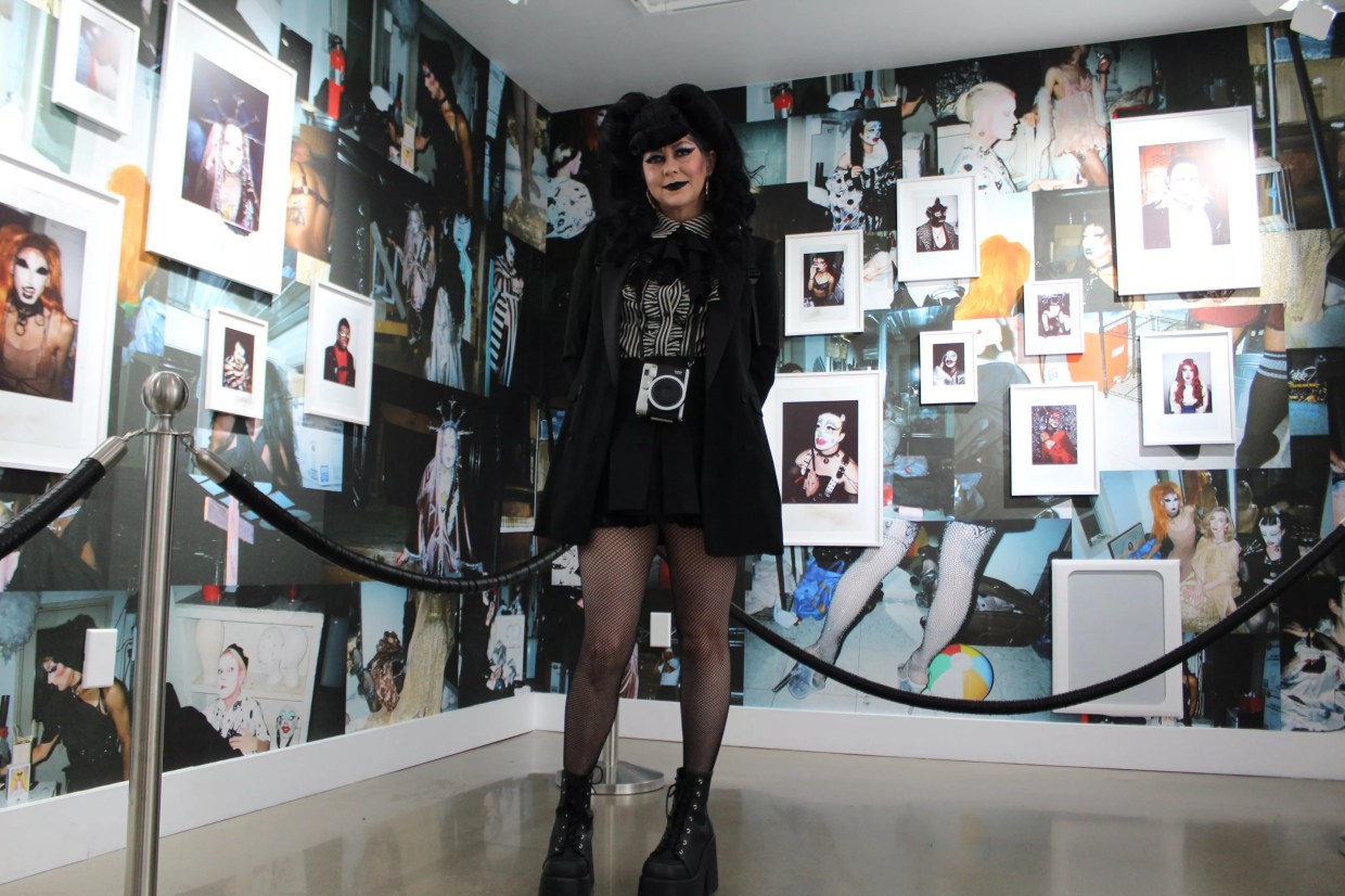 A woman dressed in black stands in front of a wall of photos