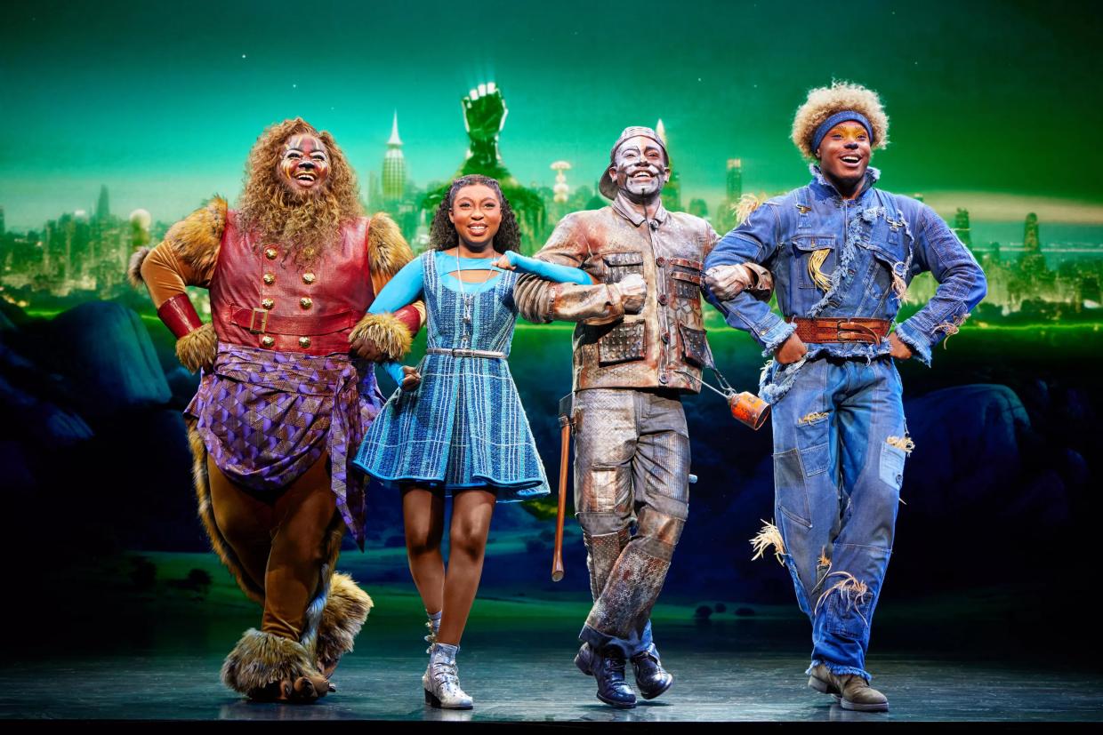 The Lion, Dorothy, Tin Man and Scarecrow walk together.
