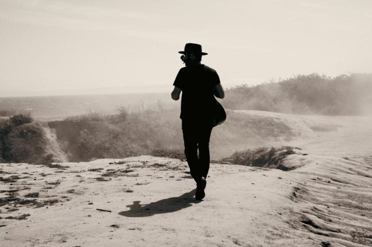 man walking around plains with a guitar strapped on his back
