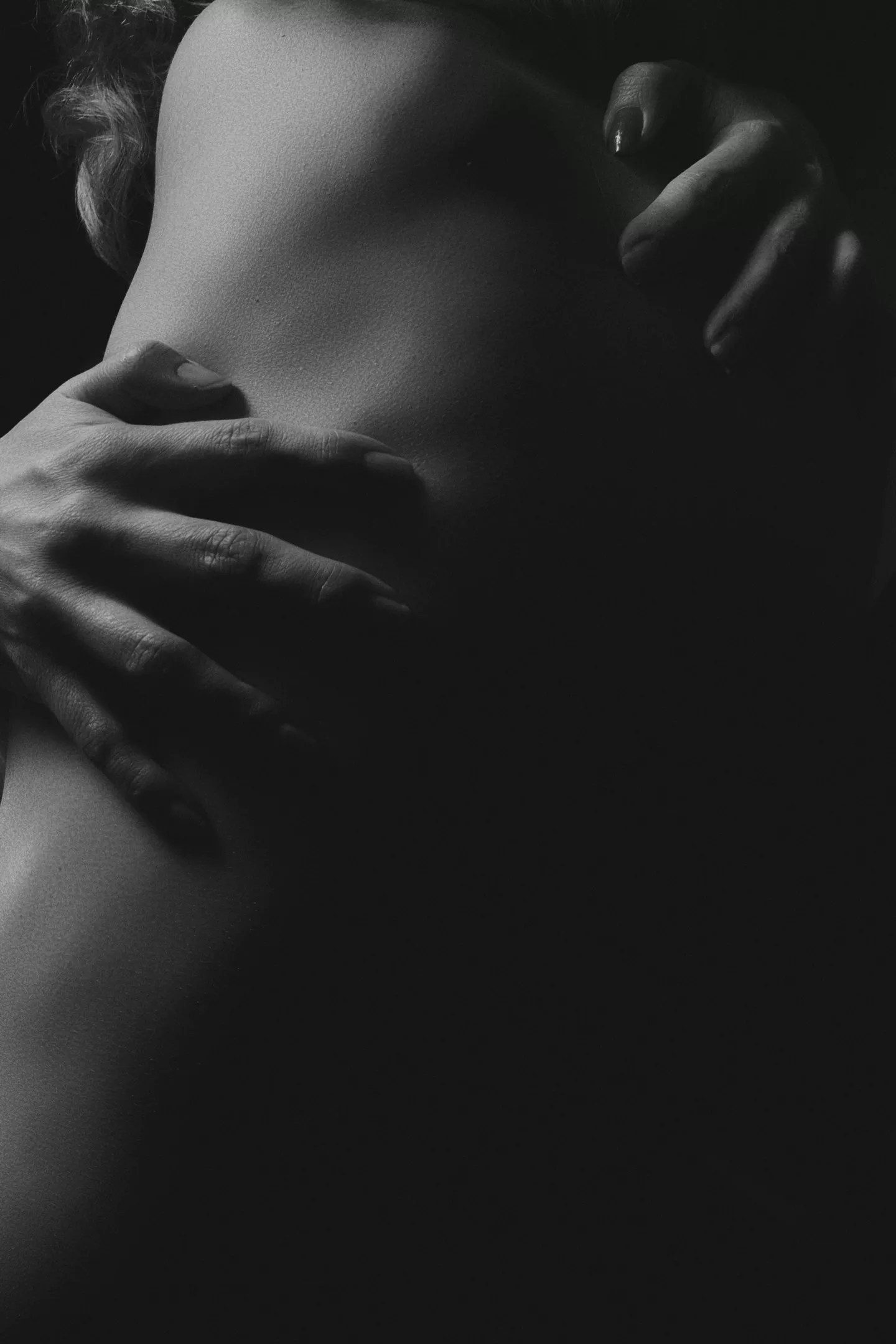 A black and white photo of hands hugging a body