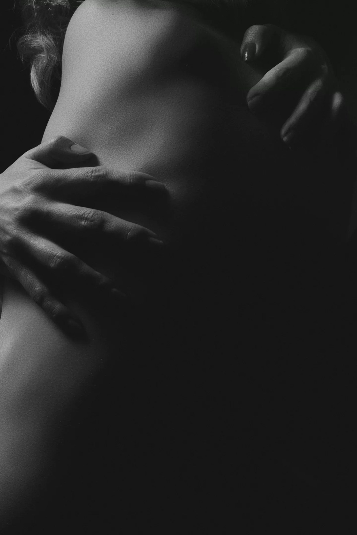 A black and white photo of hands hugging a body