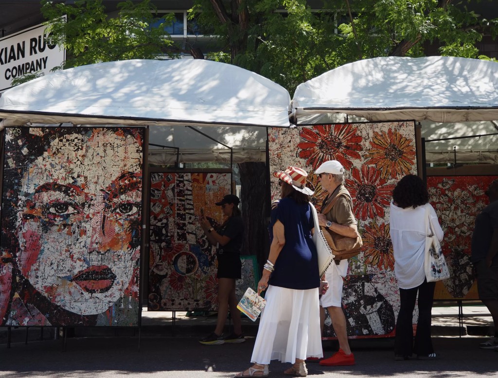 people walk past a tent of art